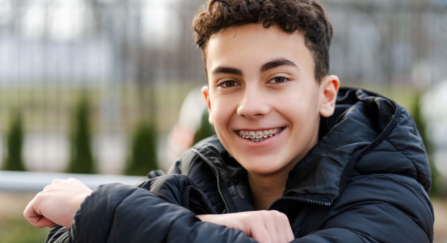 Smiling boy with braces wearing a black jacket.