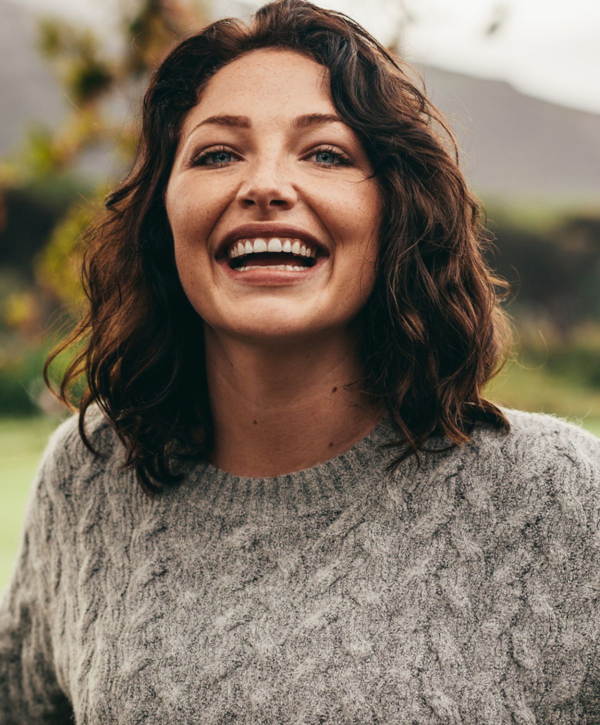 Smiling woman in a cozy sweater outdoors.