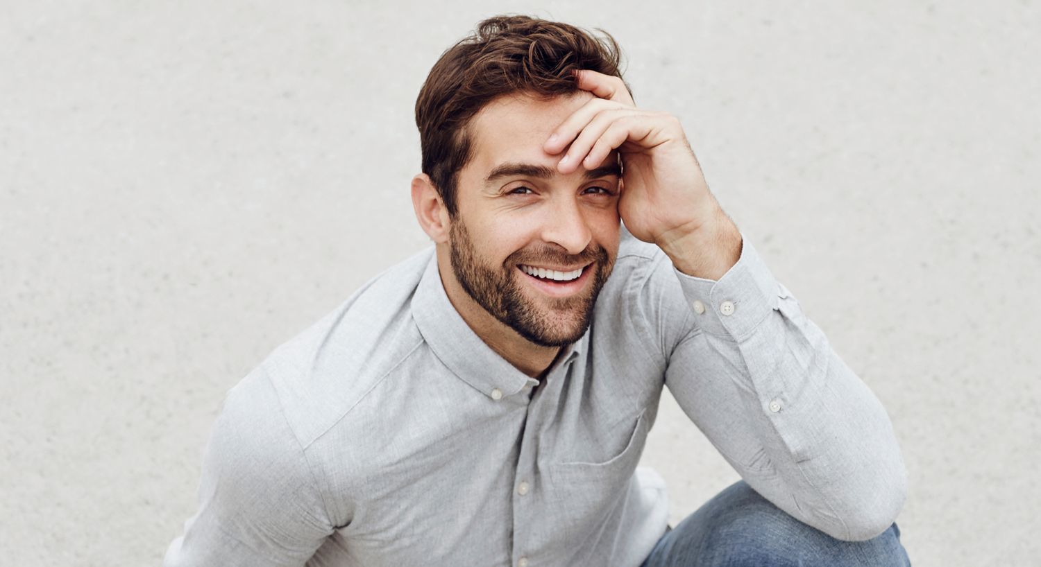 Smiling man sitting outdoors, wearing a gray shirt.