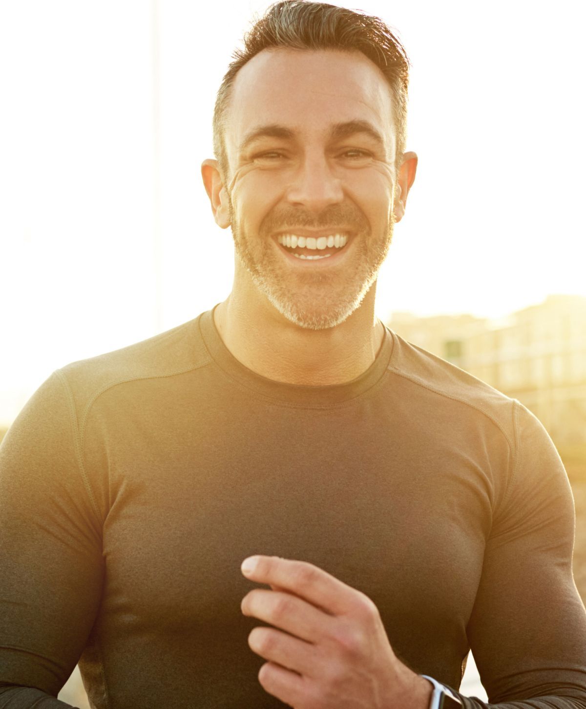 Smiling man in athletic wear outdoors, sunset lighting.