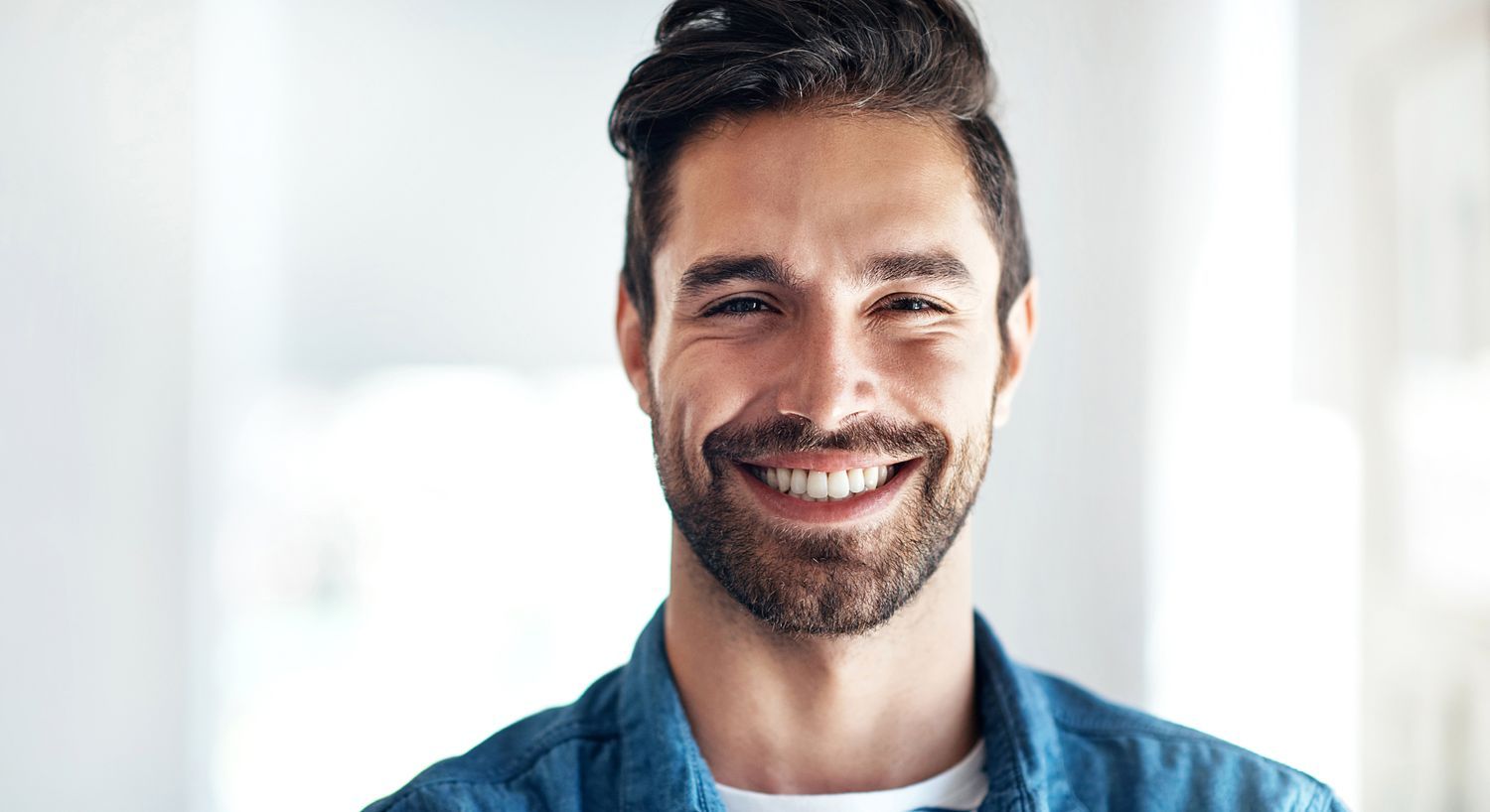 Smiling man with a beard and denim shirt.