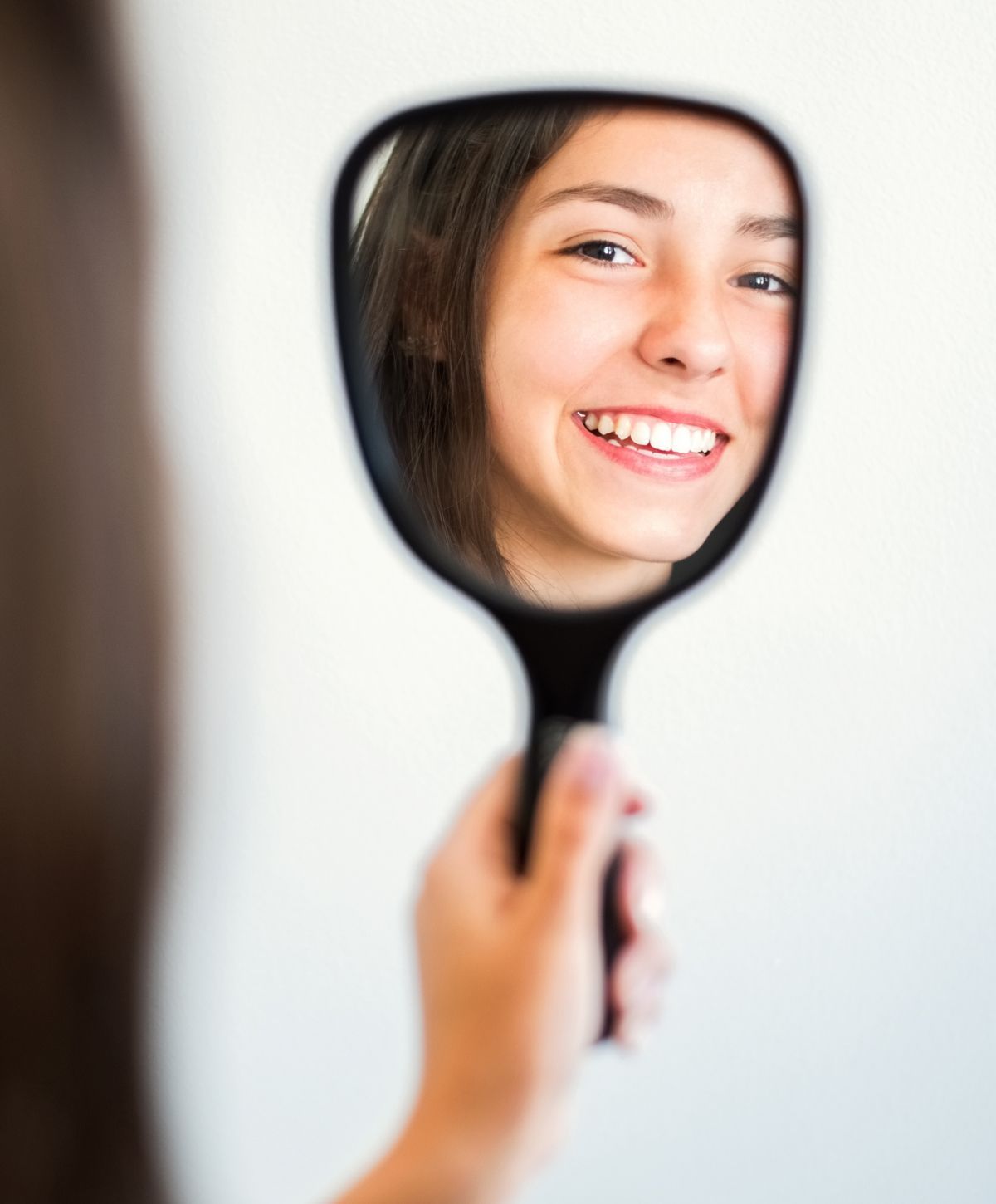 Smiling person looking into a handheld mirror.