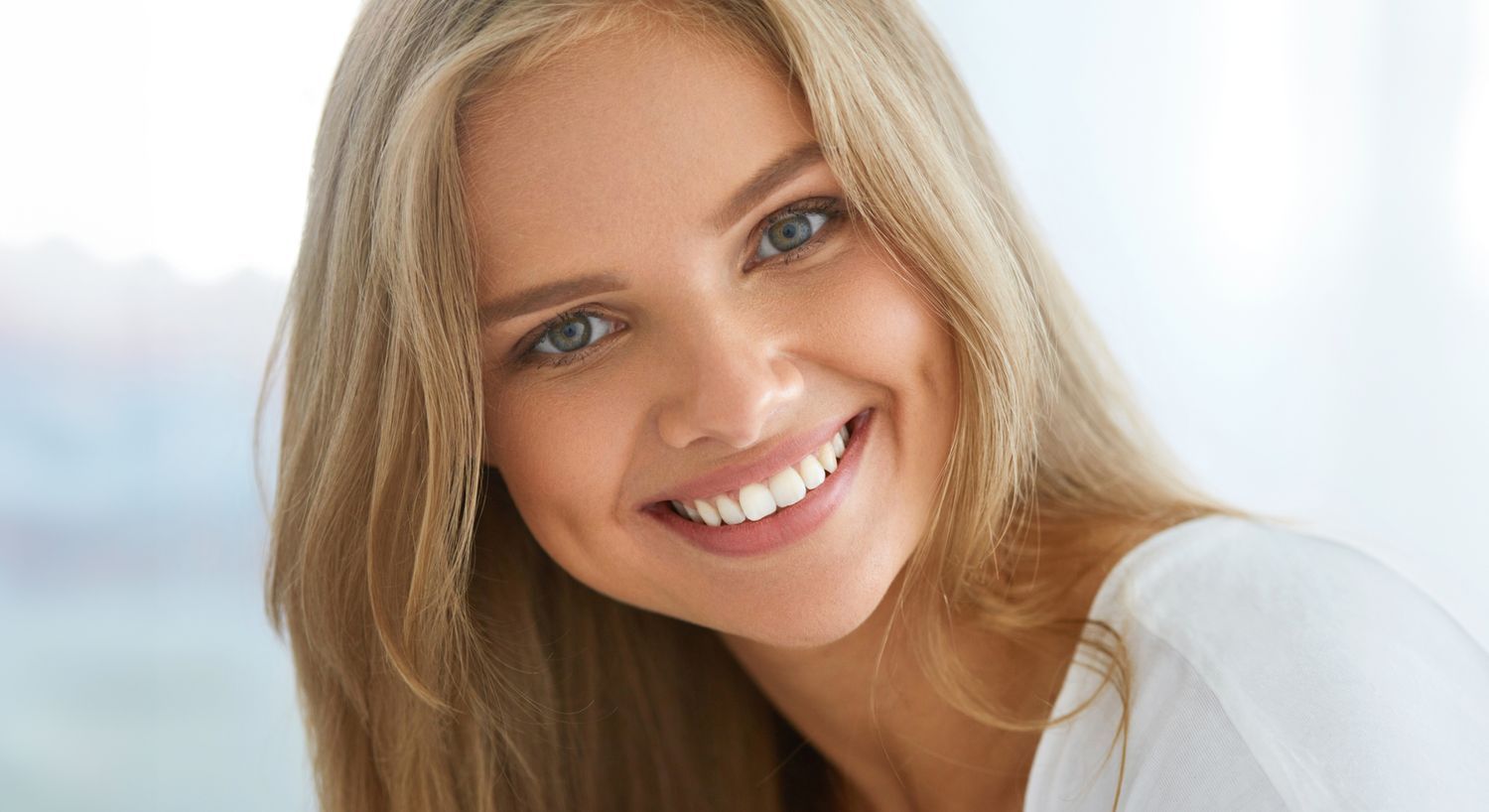 Smiling woman with long, blonde hair indoors.